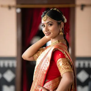 Indian woman in red and gold saree surrounded by traditional decor