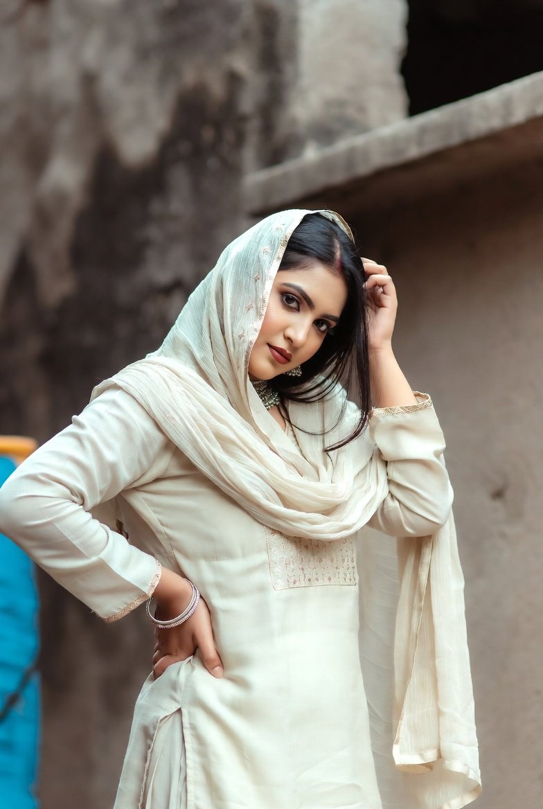 Dark-haired woman in cream cotton salwar kameez posing elegantly outdoors