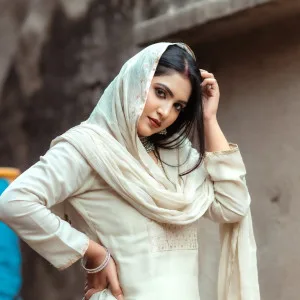 Dark-haired woman in cream cotton salwar kameez posing elegantly outdoors
