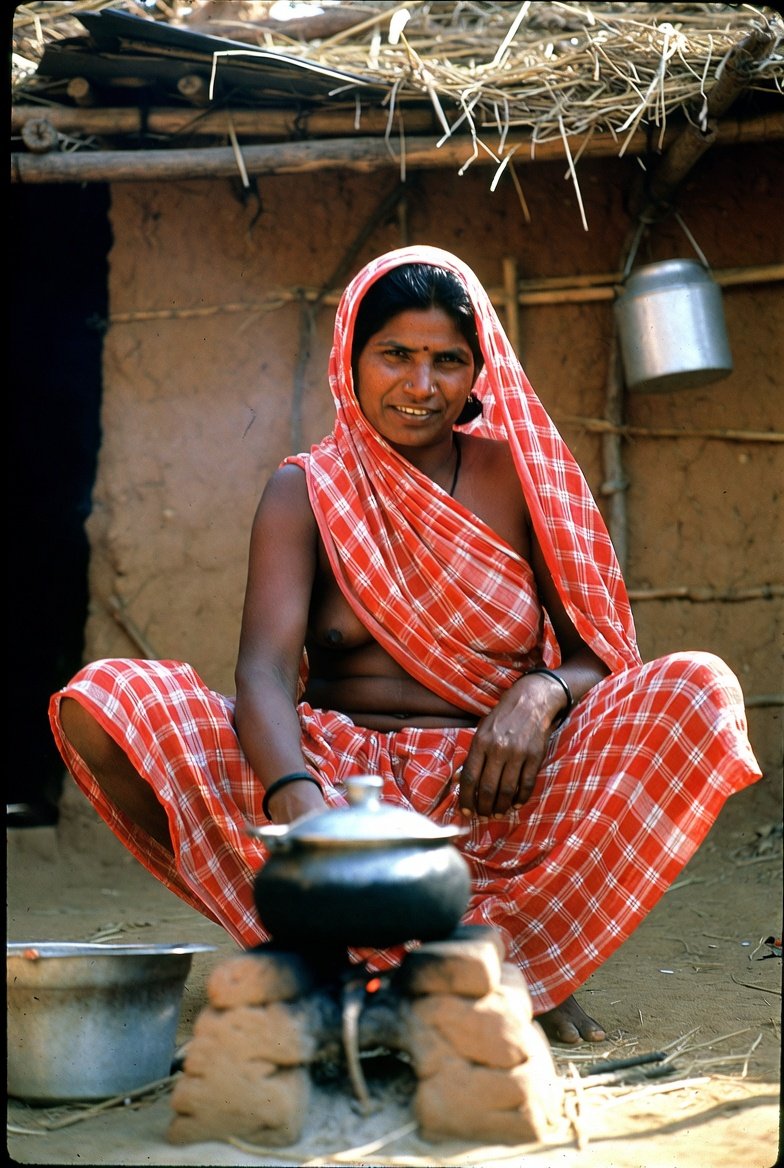 Rural Indian aunt cooking outside mud house in orange saree
